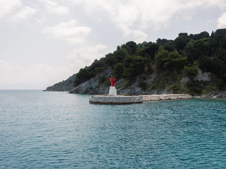 A small red lighthouse on the rocky coast of Vlorë